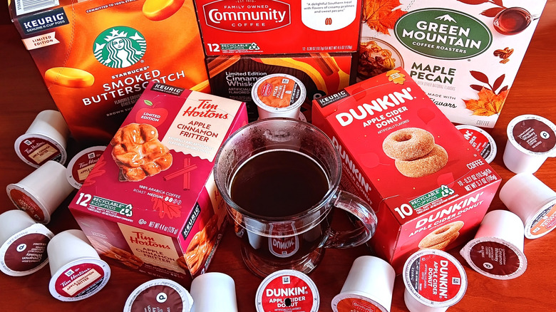 Six boxes of popular fall flavored coffee K-cups surrounded by individual K-cups and a mug of black coffee