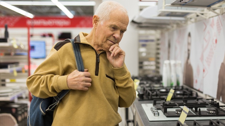 An old man examining gas stoves in a showroom