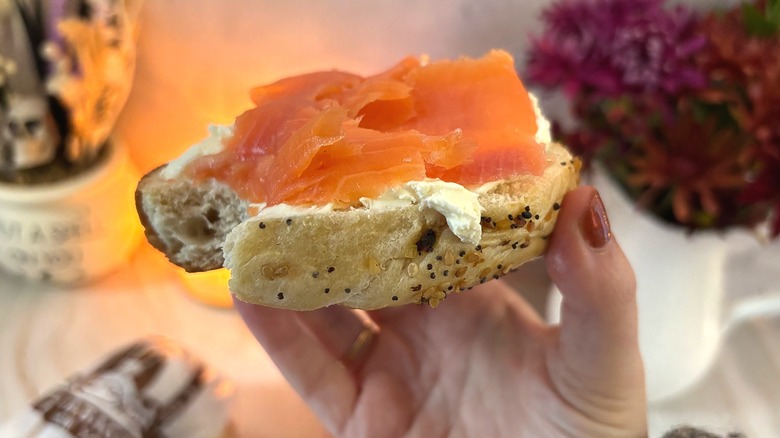 Hand holding bagel and lox with bite taken out of it