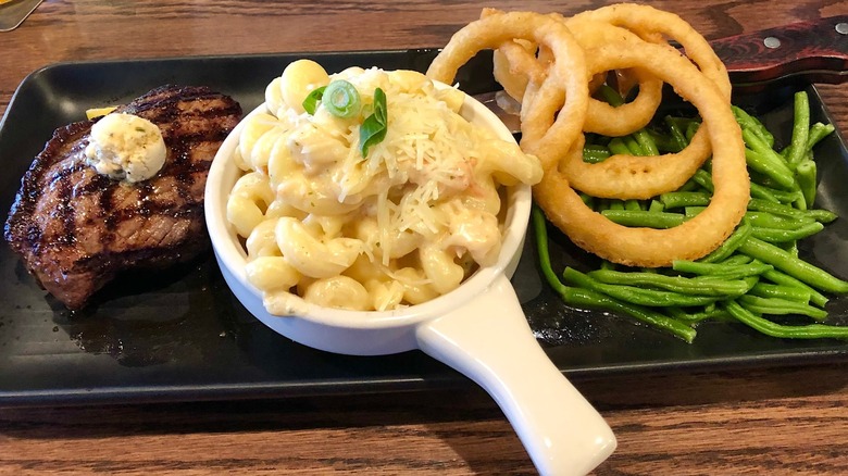 Steak dinner with mac and cheese, onion rings, and greens on a black tray