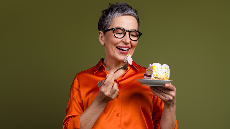 Happy woman in orange shirt green background eating cake