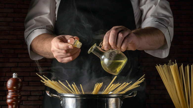 man pouring oil into boiling pot of spaghetti