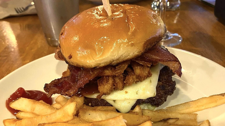 Applebee's Whisky Bacon Burger overflowing with bacon with fries and ketchup on a plate.