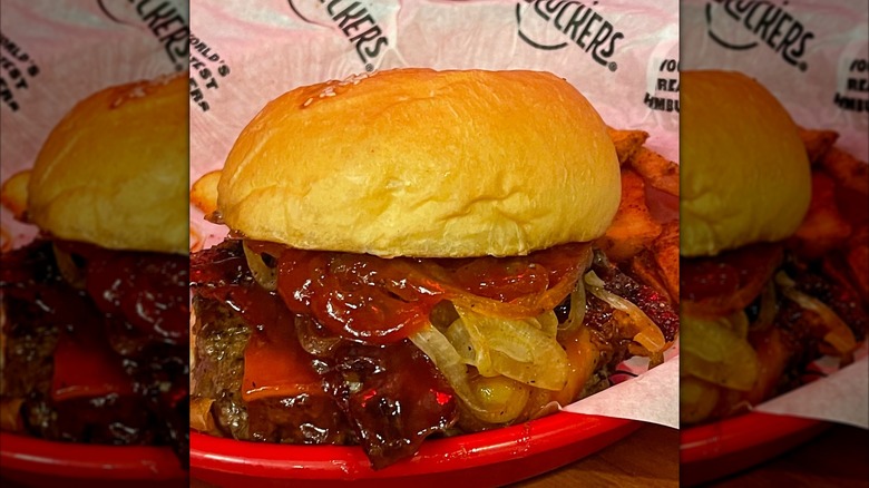 Fuddruckers Barbecue Burger overspilling with barbecue sauce and grilled onions in a Fuddruckers basket.