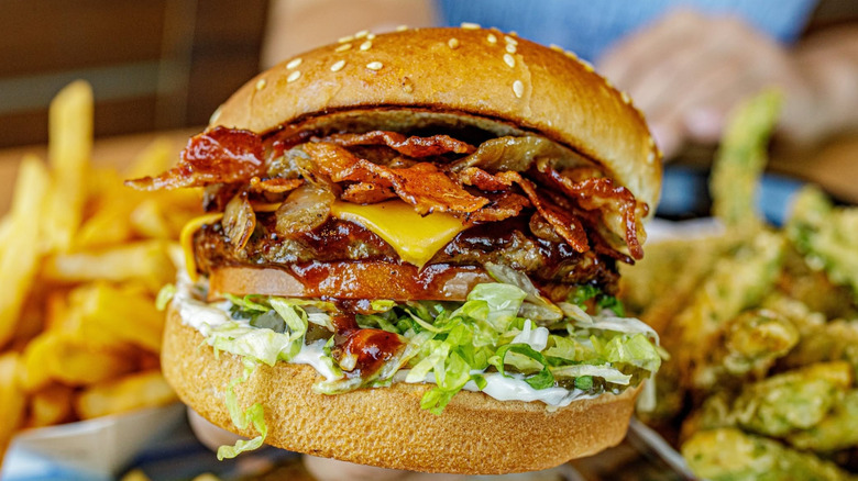 Close-up of someone holding out a Habit Burger and Grill Barbecue Bacon Char Burger.