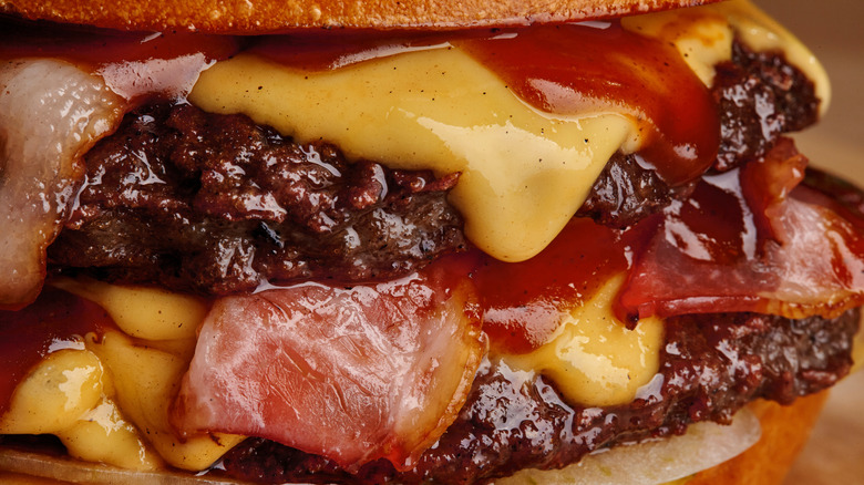 Close-up of barbecue sauce dripping between cheese laden burger patties.