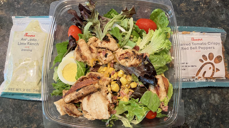 Chick-fil-A salad in plastic container with dressing and peppers either side