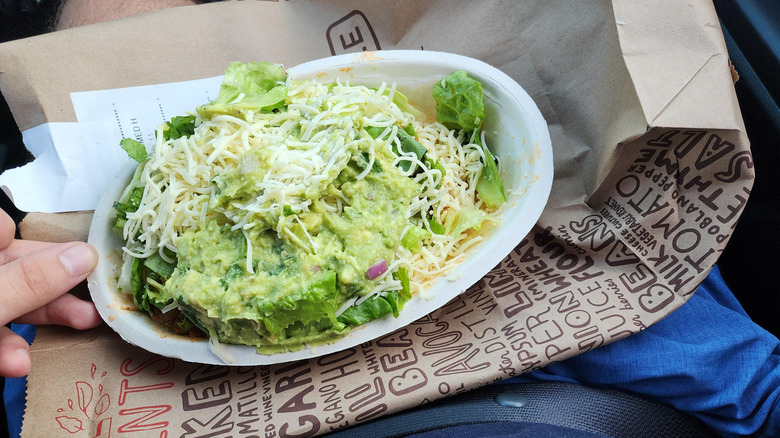 Chipotle salad on white bowl on brown paper bag on a person's lap