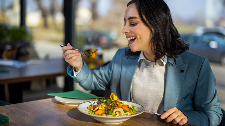 Woman smiling and eating a salad at a table outside