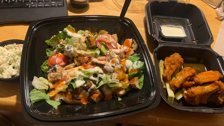 salad and chicken wings in black takeout containers at desk