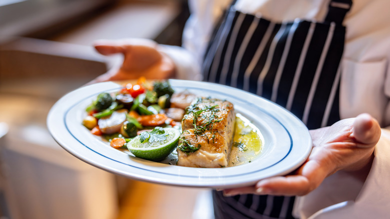 Close-up on a server holding a fish dish at a restaurant