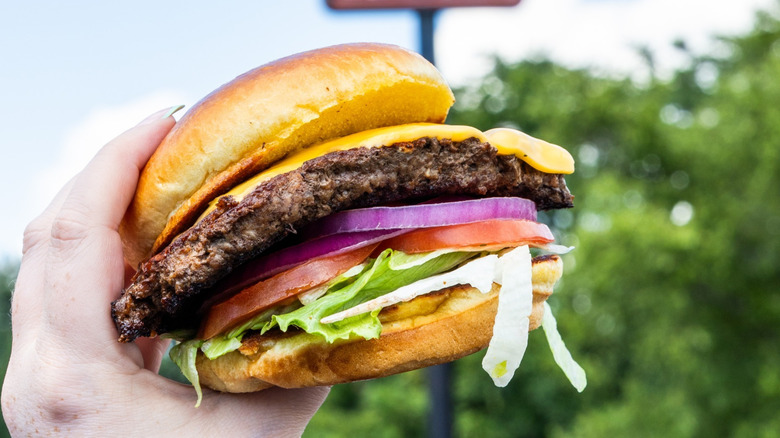 A hand holding an All-American Cheeseburger from Texas Roadhouse