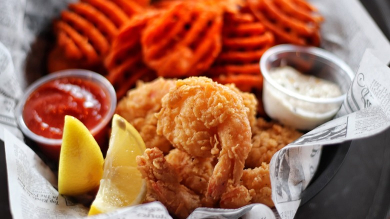 Fried shrimp basket with lemon, waffle fries, and dips at Hook & Reel Cajun Seafood & Bar