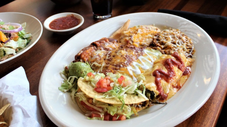 Combo platter with assorted Tex-Mex items on table with salad and salsa