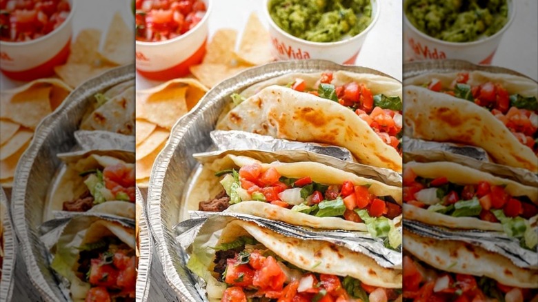 Tacos in tray with tortilla chips and cups and guacamole and salsa