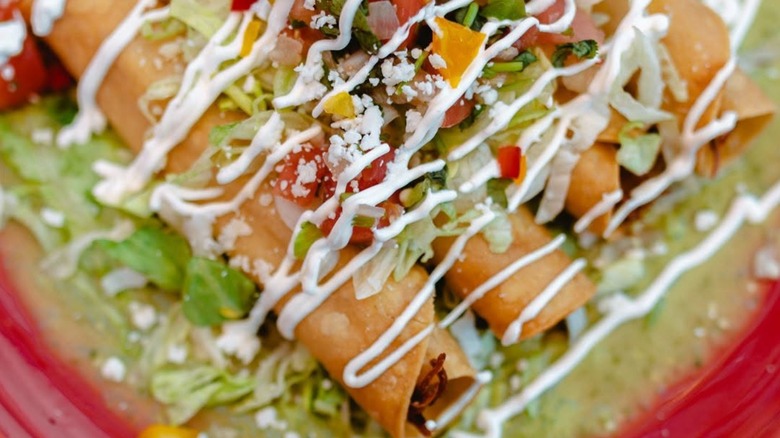 Taquitos on plate with lettuce, sour cream, and salsa
