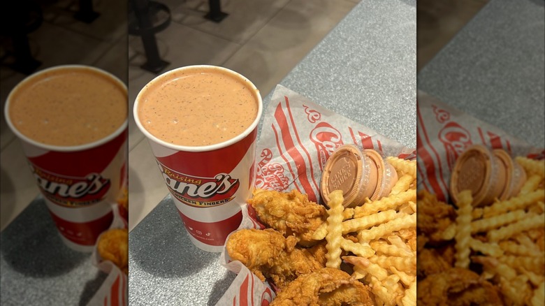 A large fountain drink cup of Cane's sauce next to a chicken finger combo in a basket.