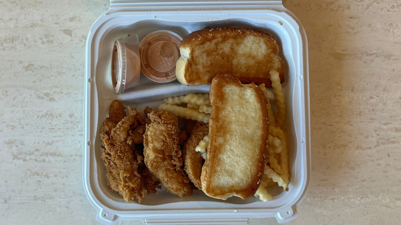 An aerial view of a Raising Cane's Caniac combo, consisting of chicken fingers, Texas toast, fries, sauce, and slaw, in a white plastic container on a table.