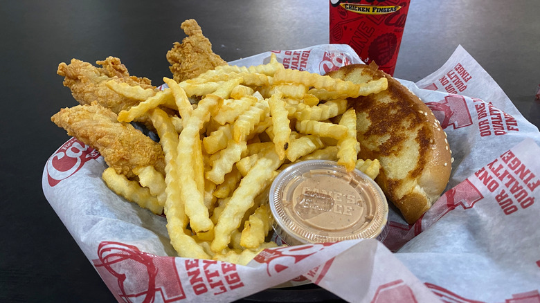 A Raising Cane's chicken combo prominently showing a small plastic cup of the pink Cane's Sauce in the foreground.