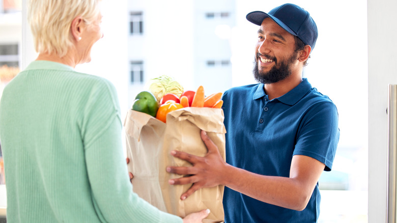Grocery delivery man handing brown paper bag of food to woman