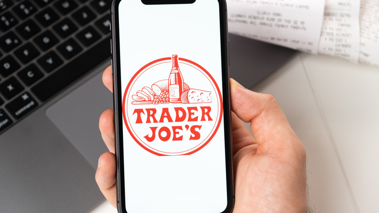 Trader Joe's logo on phone screen, laptop in background