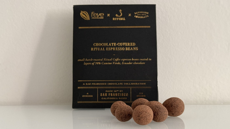 Chocolate covered espresso beans with dusting of cocoa powder in front of elegant pouch