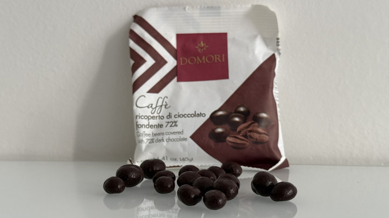 Dark chocolate covered espresso beans on table in front of Domori paper pouch