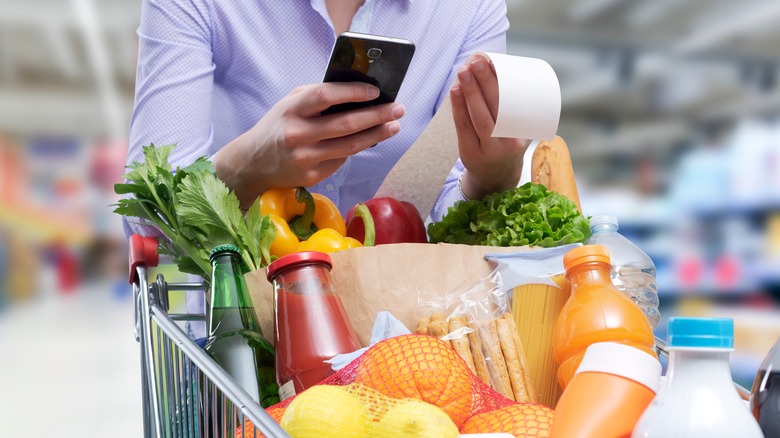 Woman with cart full of groceries checking her receipt