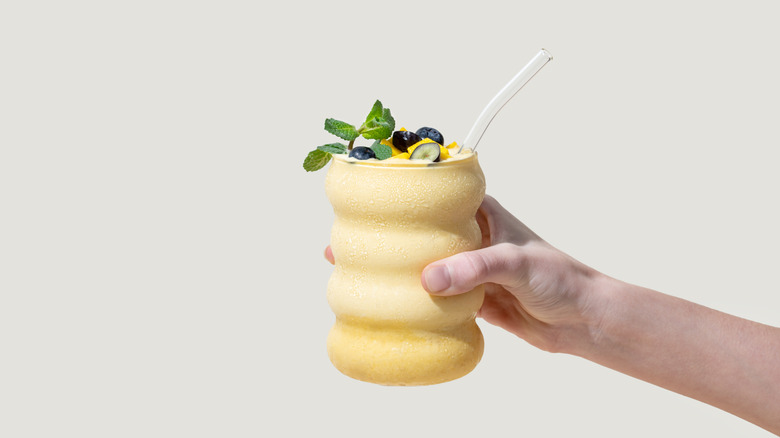 hand holding yellow fruit smoothie on white background