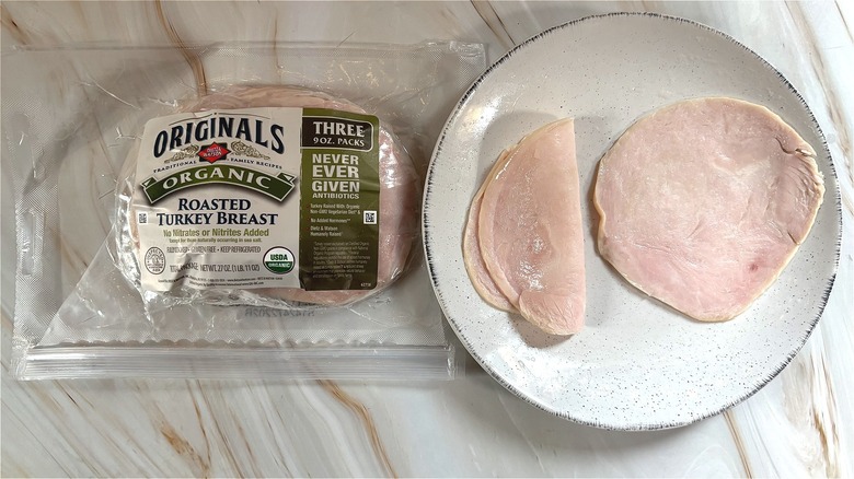 Slices of Dietz & Watson organic sliced roasted turkey on white plate next to package on table