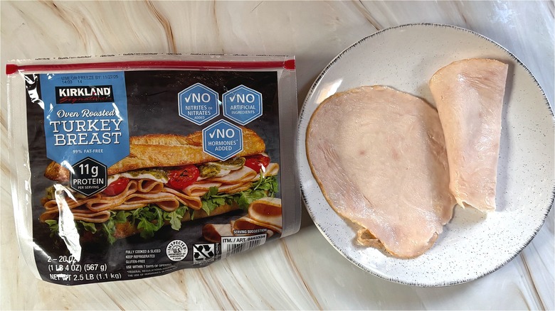 Slices of Kirkland oven-roasted turkey breast on white plate next to package on table