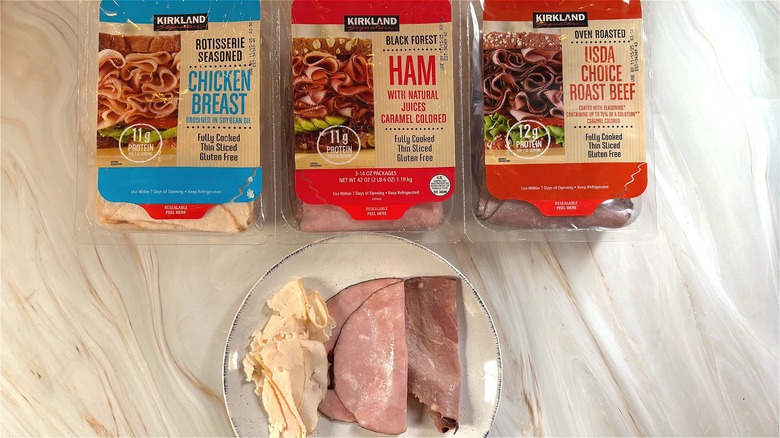 Slices of Kirkland chicken breast, ham, roast beef on white plate next to variety deli meats package on table