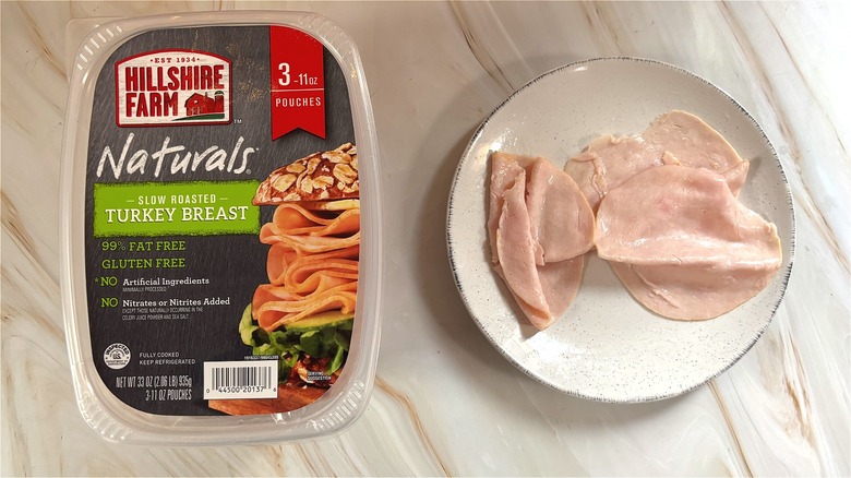 Slices of Hillshire Farm Oven-roasted turkey breast on white plate next to package on table