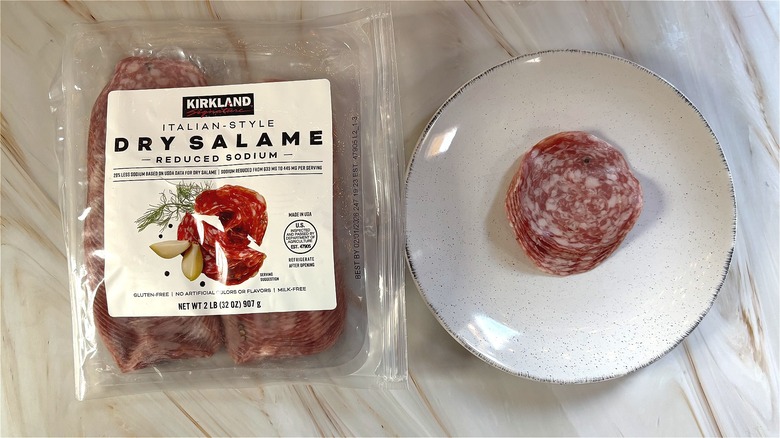 Slices of Kirkland Italian-style dry salame on white plate next to package on table