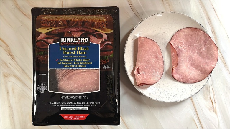 Slices of Kirkland uncured black forest ham on white plate next to package on table