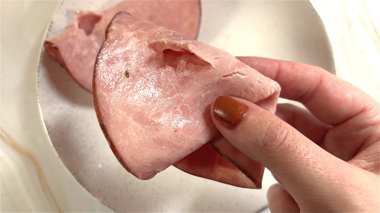 Hand holding slice of Kirkland uncured ham over white plate