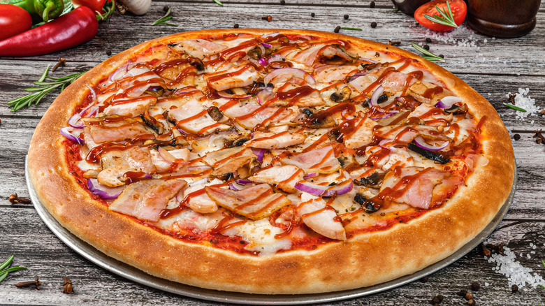 Thick-crust pizza with slices of meat and drizzle of red sauce on top