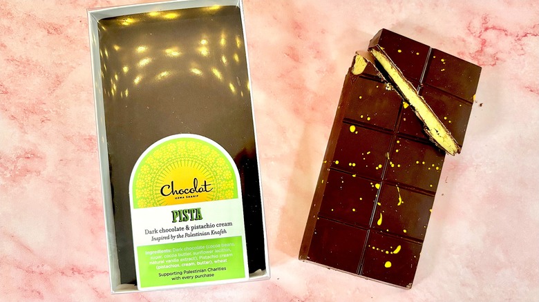 Chocolat Uzma Dubai chocolate package next to bar on pink marble surface