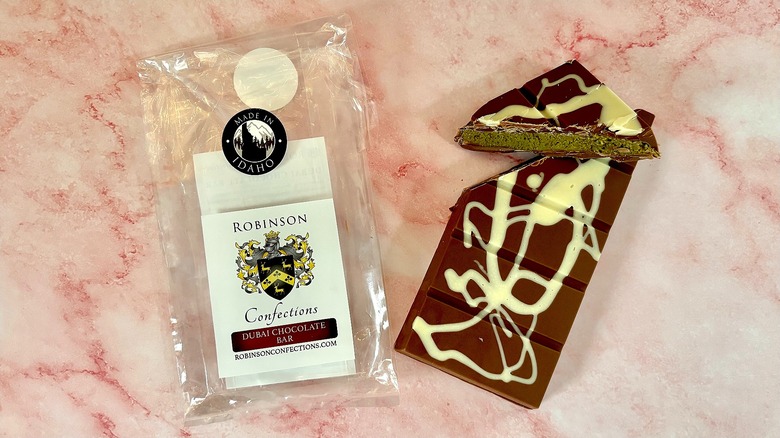 Robinson Dubai chocolate package next to bar on pink marble surface