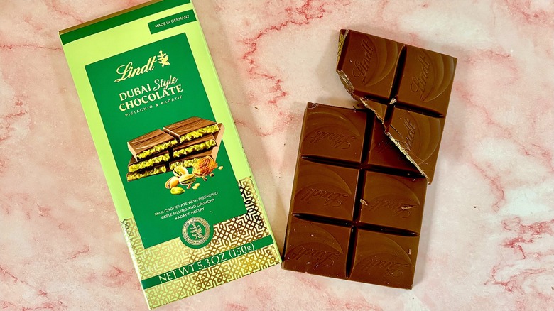 Lindt Dubai chocolate package next to bar on pink marble surface