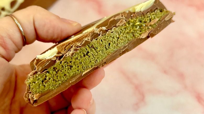 Close-up of interior of Dubai chocolate bar, held in hand over pink marble surface