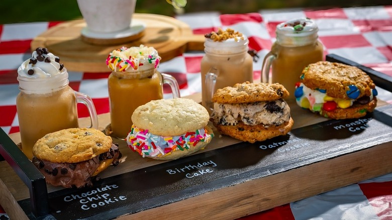 Row of cookie sandwiches in front of milkshakes on checkered tablecloth
