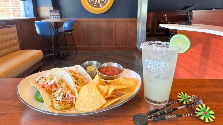 Plate of tacos on wooden table next to salt-rimmed cocktail and darts