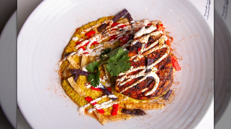 Close-up of plated dish with red pepper seasoning, parsley leaves, and cream sauce drizzle, in white bowl
