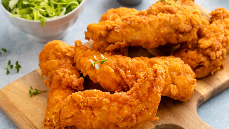 a plate of chicken tenders with salad and dip