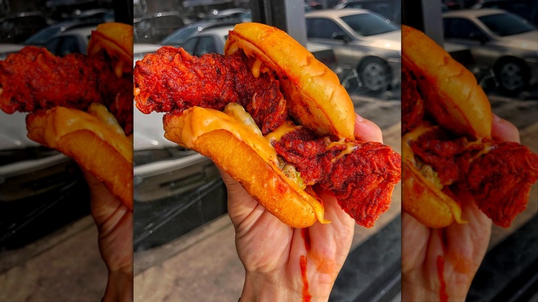 Hand holding dripping Dave's Hot Chicken slider