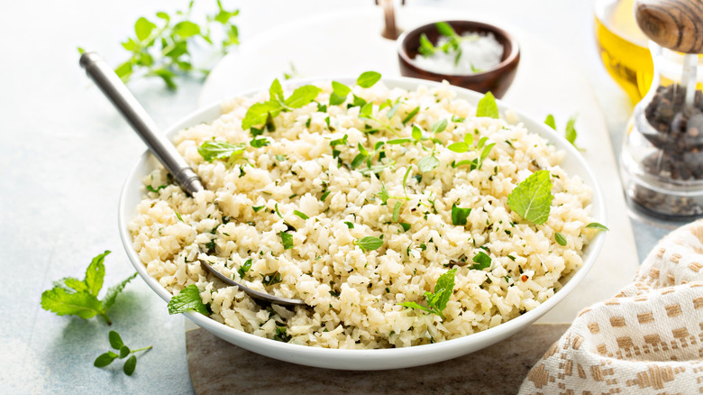 Cauliflower rice in a white bowl with fresh mint on top