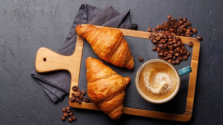 Croissants, coffee beans, and a cup of coffee on a slate and wood serving board