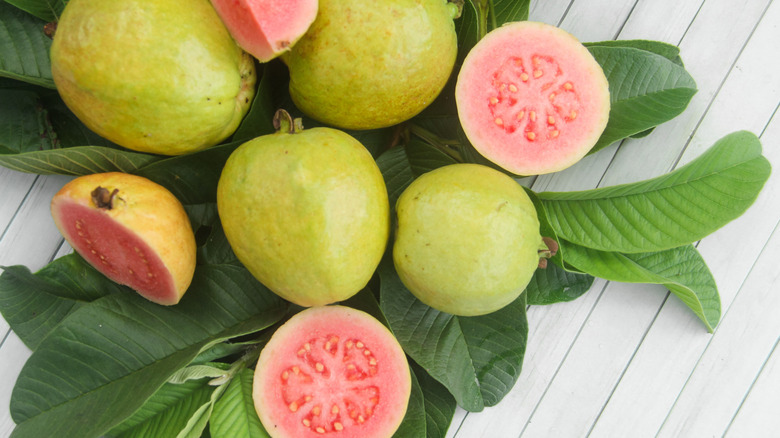 Whole and halved guavas on top of leaves on a white wooden table