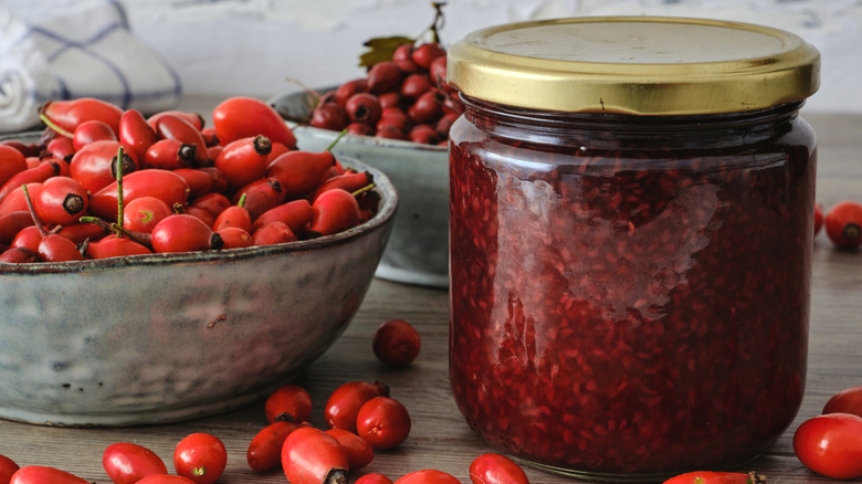 Two bowls of rosehips next to a jar of red jam